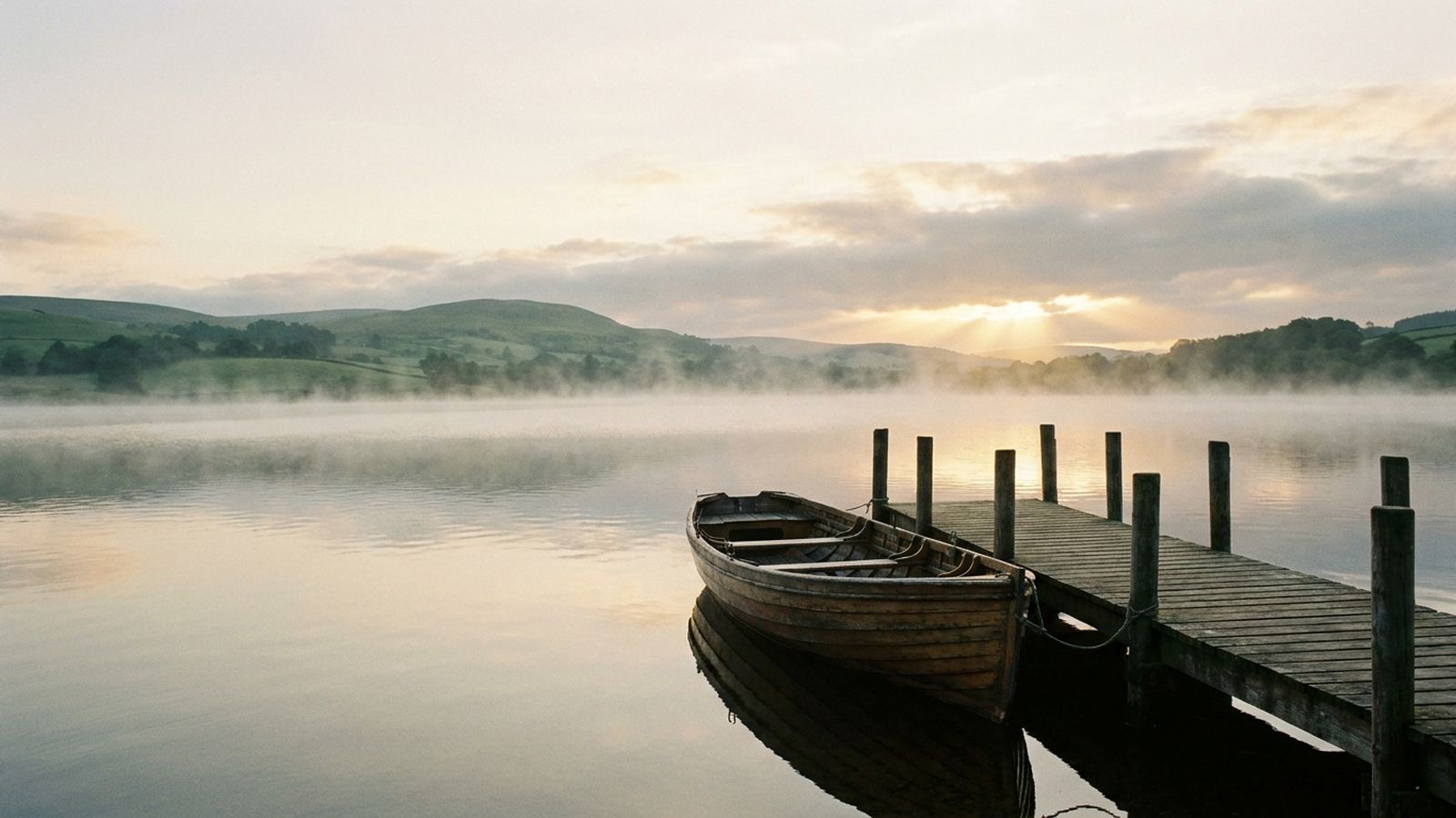 A rowing boat moored at a jetty on a calm lake at dawn